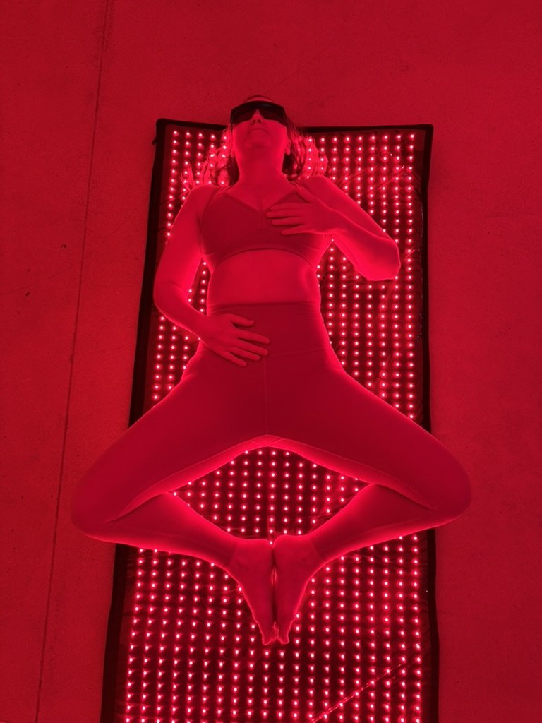 A student resting in reclined butterfly on a glowing red light therapy mat