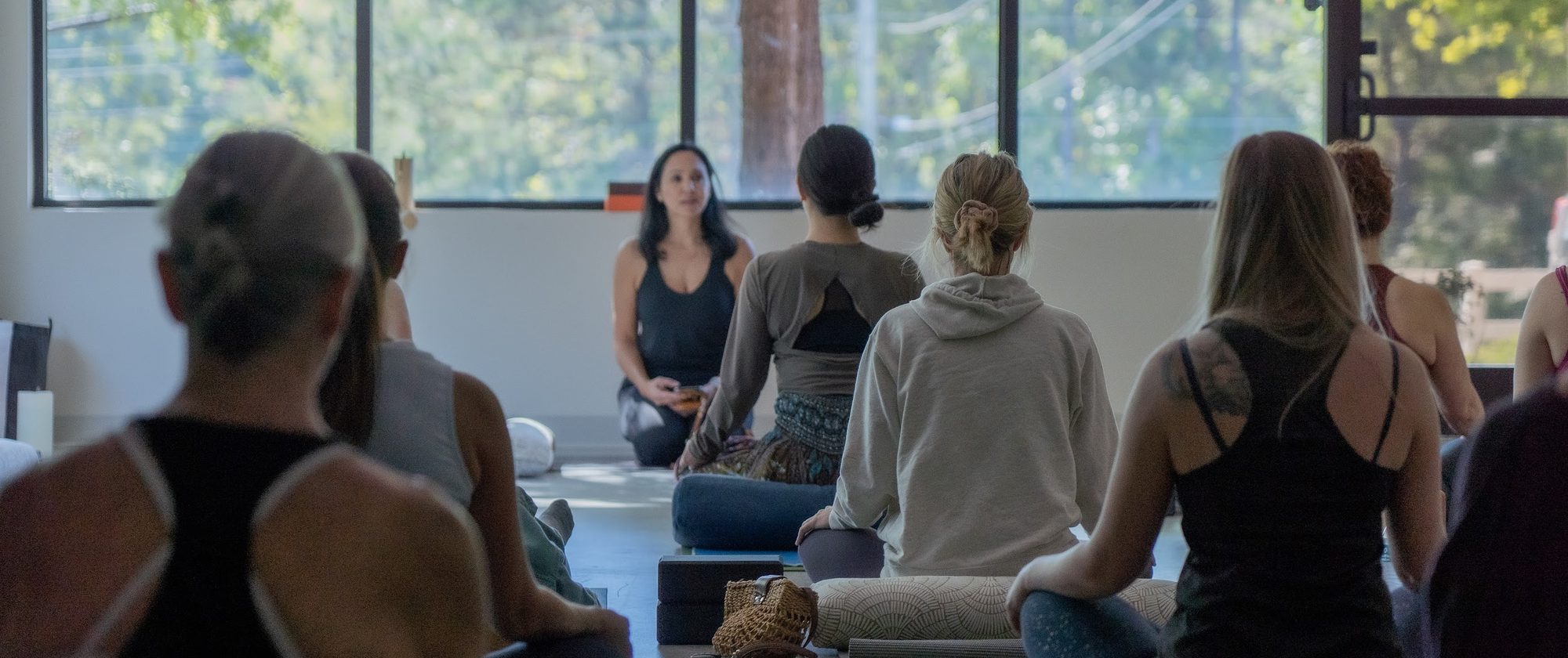 A small group seated on their mats, listening to the teacher at the front of the studio